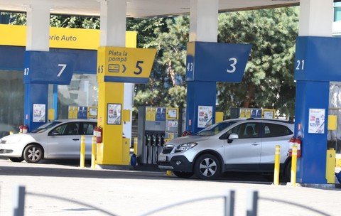 Imaginea prezintă o stație de carburanți cu mai multe pompe numerotate, unde sunt parcate două autoturisme pentru alimentat.