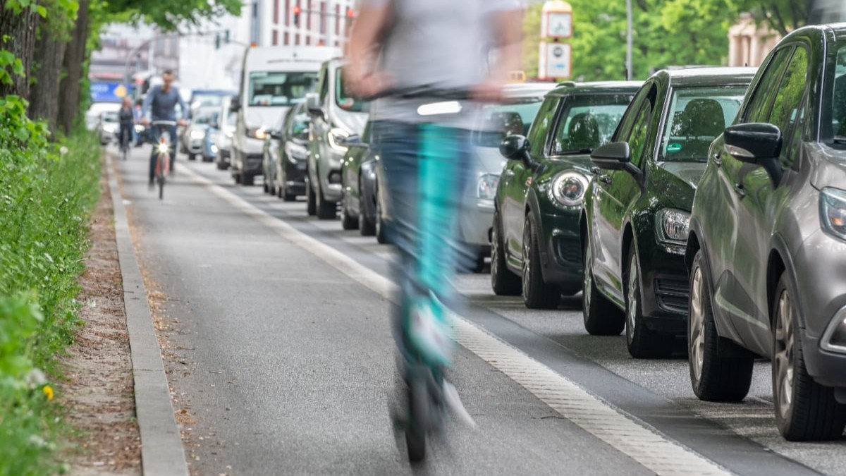 Un bărbat care merge pe o trotinetă electrică pe stradă și depășește mai multe mașini