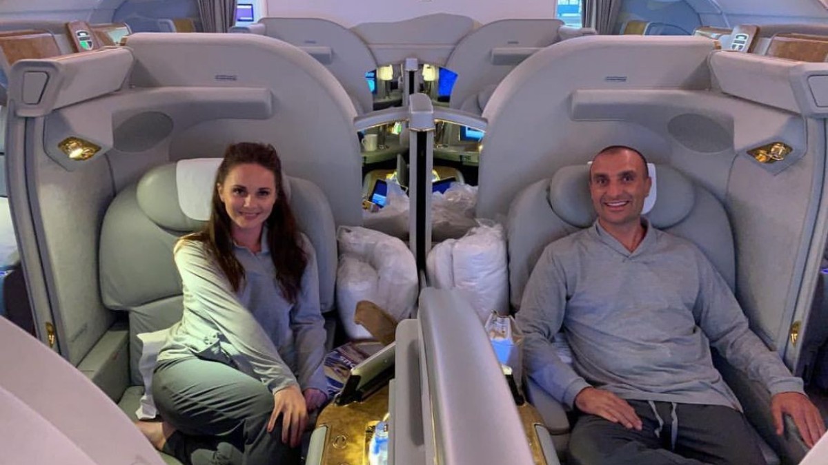 Un bărbat și o femeie la bordul unui avion, stau în fotoliile de la Clasa I și zâmbesc în fața camerei