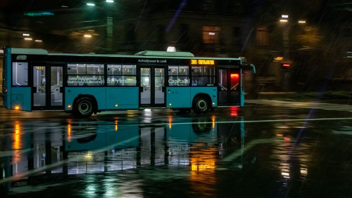 Autobuz STB, de culoare albastră, pe timp de noapte și ploaie, într-o intersecție din București
