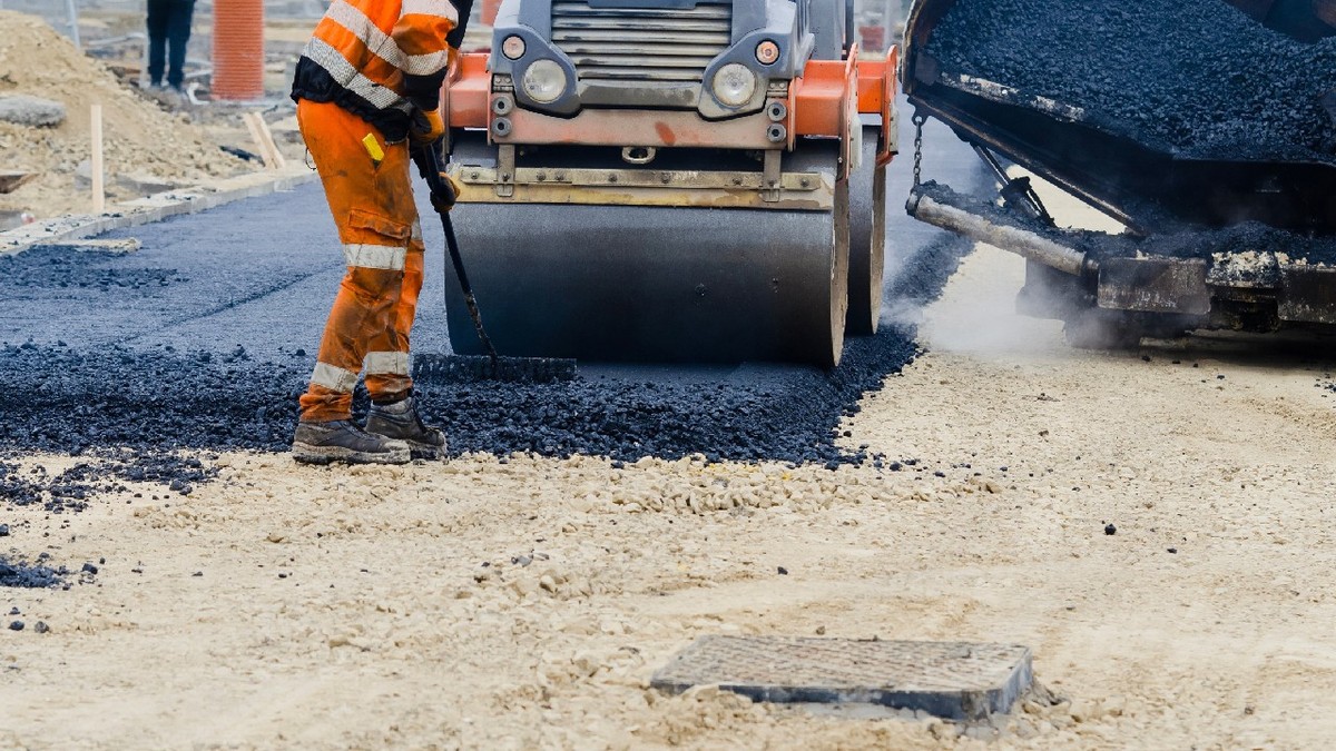 Lucrătorii din construcții în echipamente de înaltă vizibilitate aplică asfalt proaspăt fierbinte pe suprafața drumului