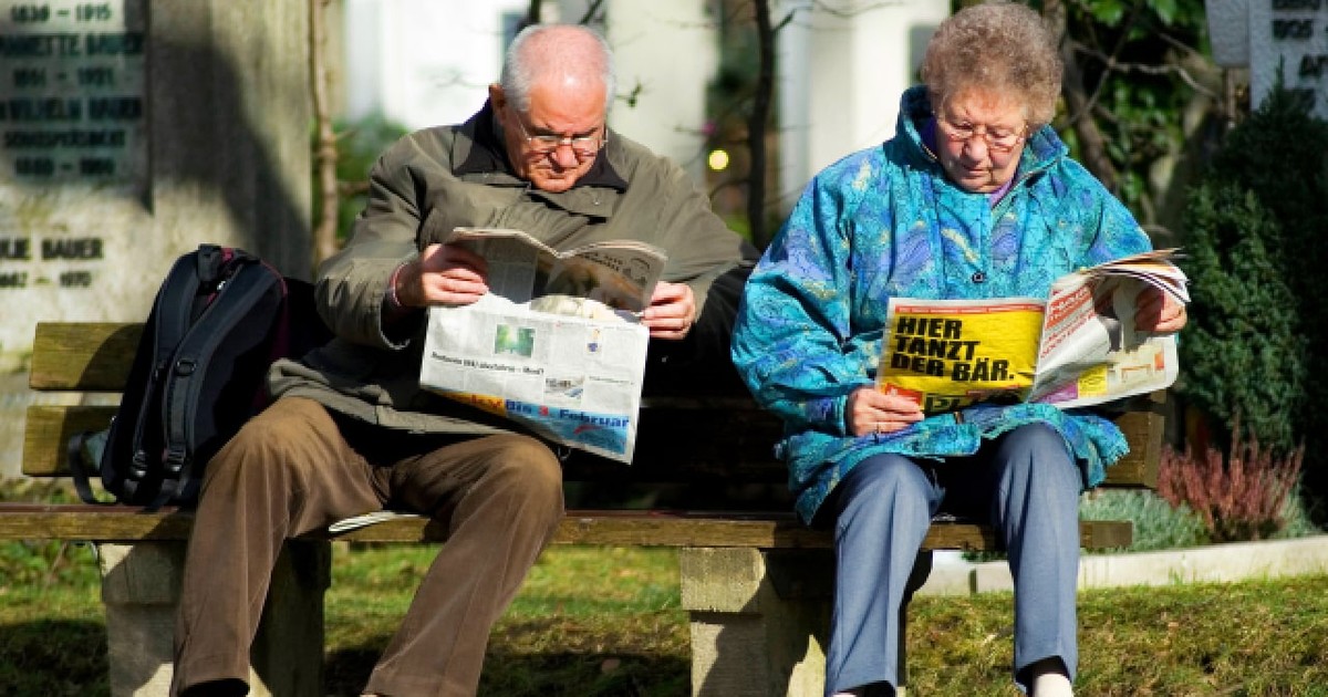 München, Bavaria, Germania, 18 martie 2007: un cuplu de pensionari stând relaxat pe o bancă din parc, bucurându-se de primele raze calde de soare și citind ziarul