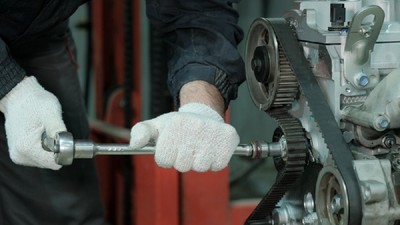 Un mecanic strânge șuruburile kitului de distribuție pe curea al unui motor auto