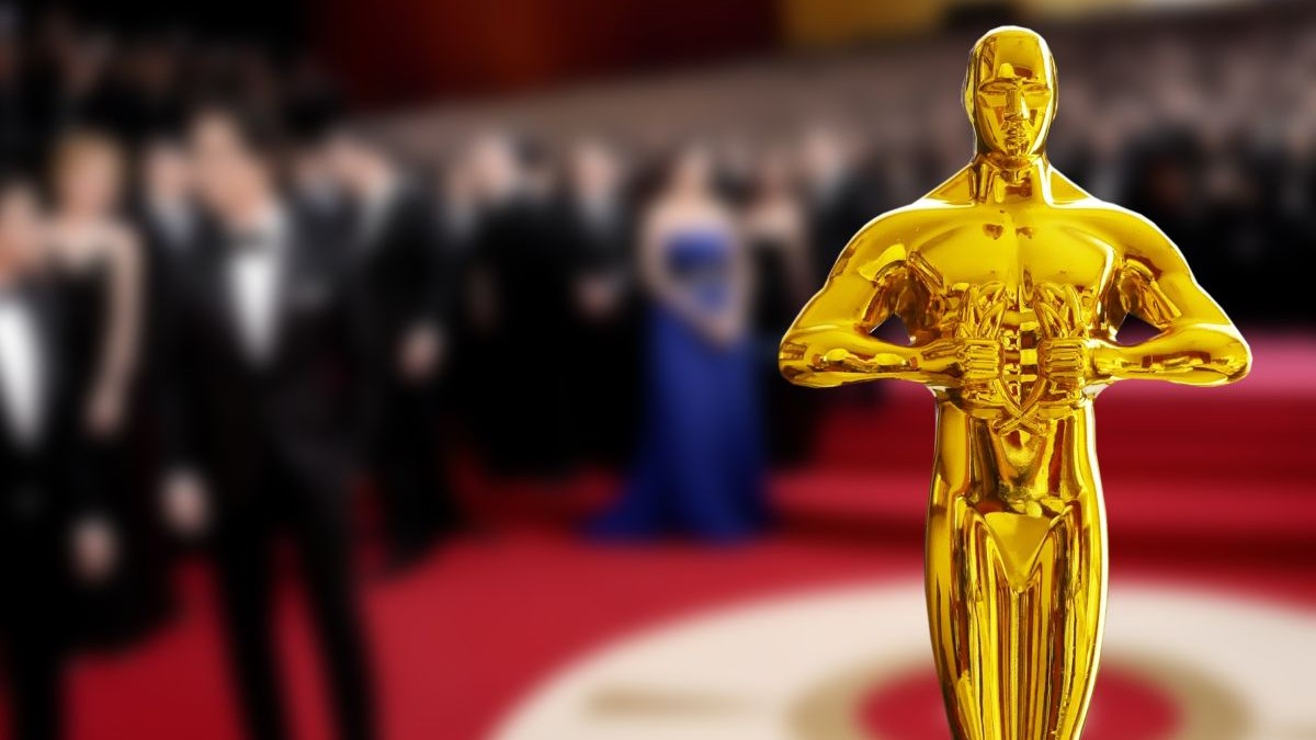 Statuia de aur de la Hollywood, cu fundal de ceremonie de premiere, se vad multe persoane la ceremonie, pe covorul rosu, dar fundalul este neclar,