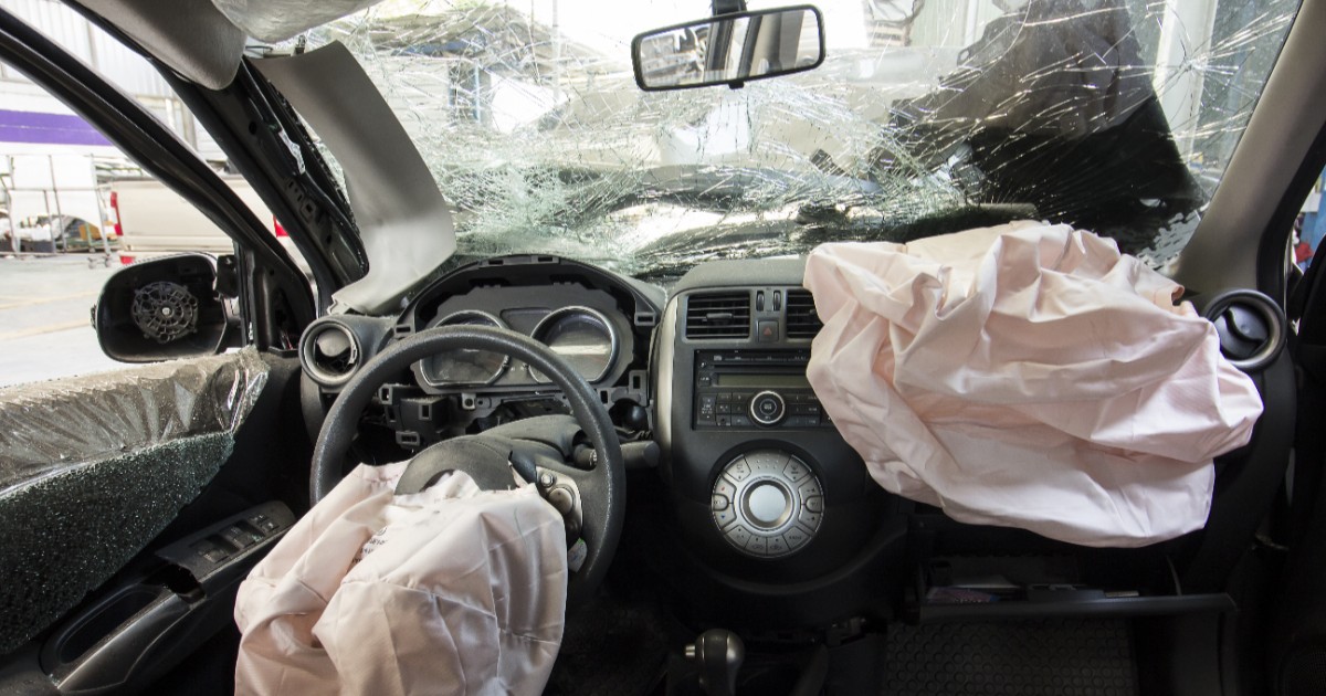 Imaginea prezintă interiorul puternic avariat al unui autoturism în urma unui accident, având parbrizul spart și airbagurile declanșate.