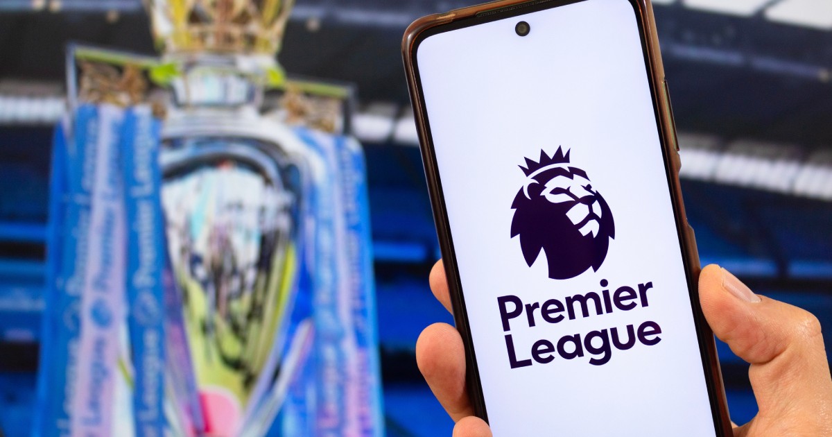 Un telefon pe ecranul căruia este scris „Premier League”. În fundal, cupa Premier League