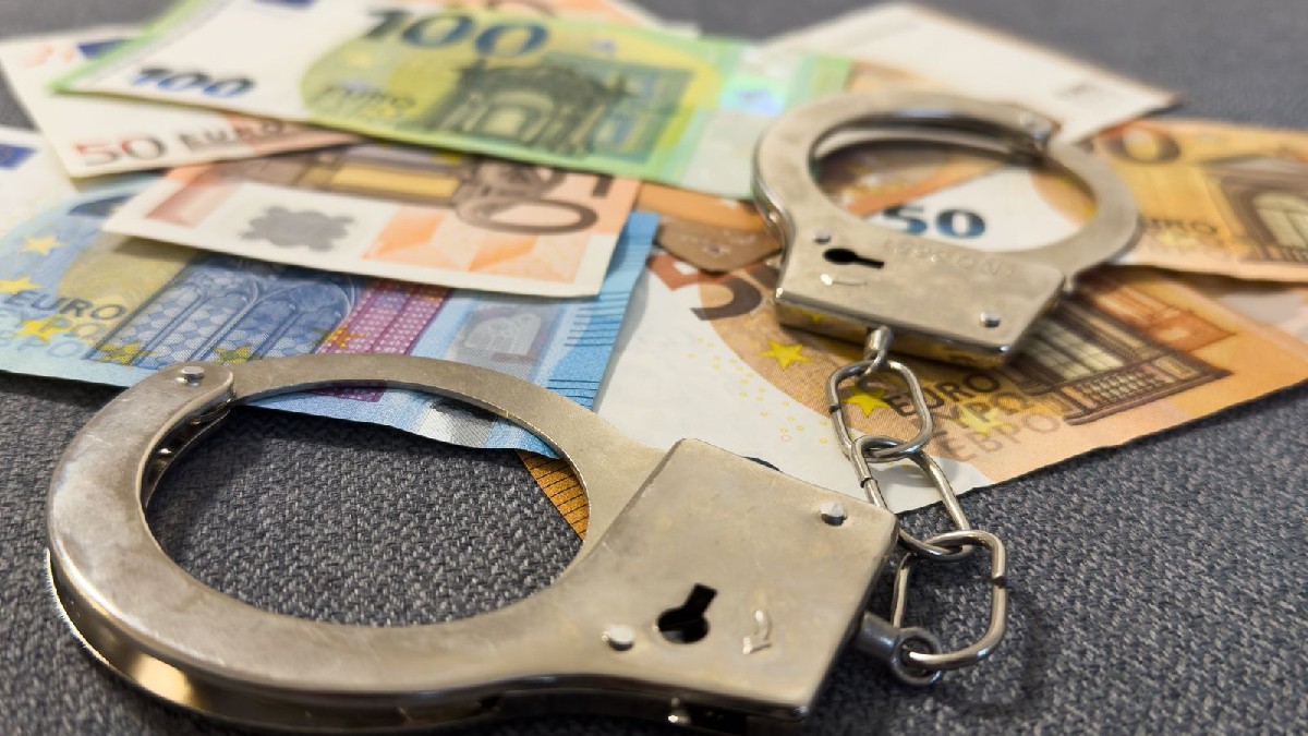 O pereche de cătușe metalice așezate peste mai multe bancnote euro de diferite valori.