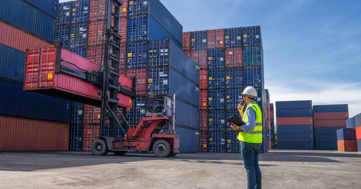 Un angajat cu vestă reflectorizantă, în timp ce se ocupă de așezarea containerelor ce transportă produse din China, într-un port