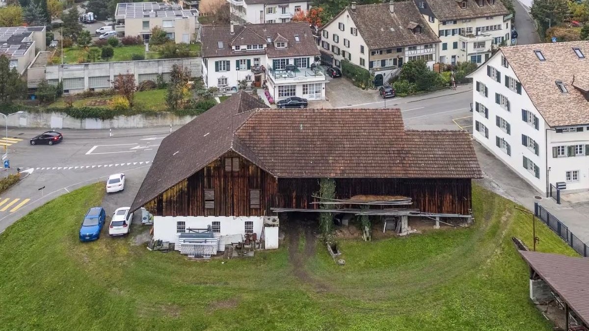 Fotografie aeriană a unui orășel elvețian pitoresc, cu un hambar rustic din lemn, înconjurat de case cu acoperișuri înclinate și frunziș colorat de toamnă.