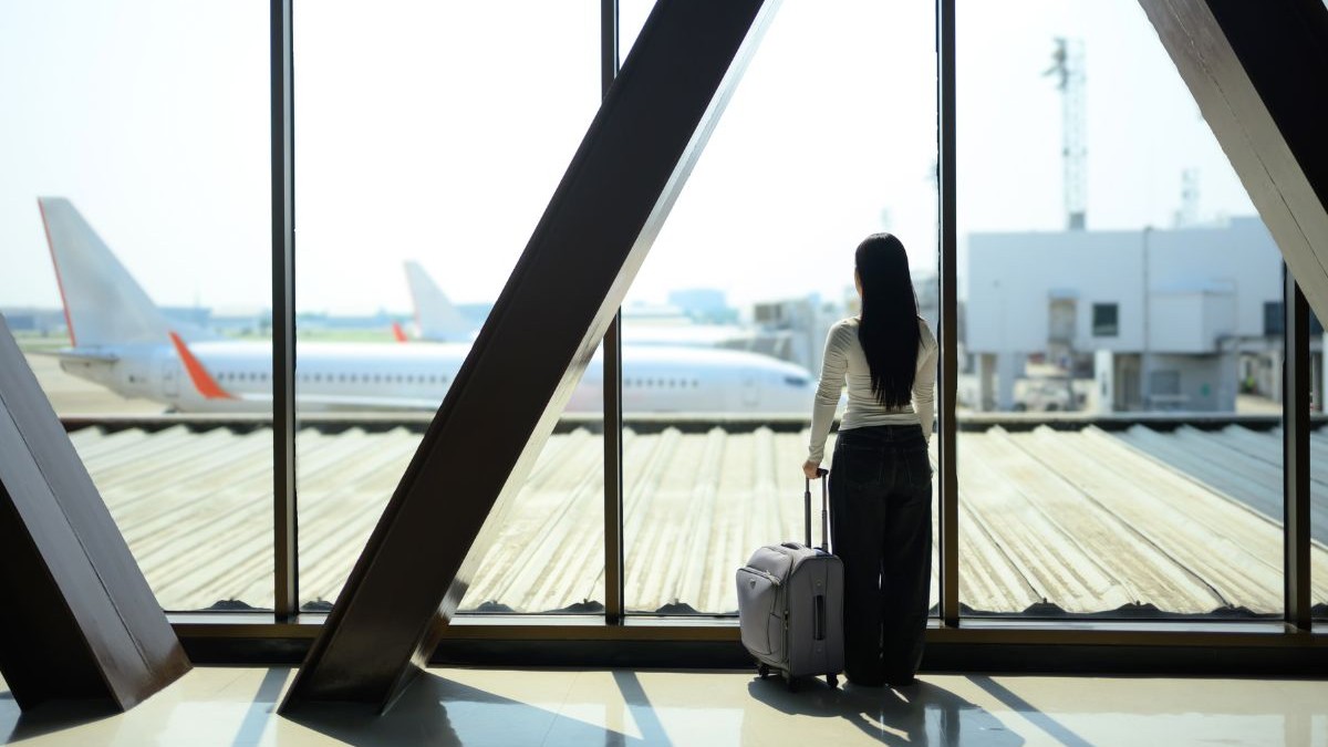 O tânără din Generația Z, aflată în călătorie, așteaptă cu valiza în mână, privind avionul de la fereastra aeroportului.