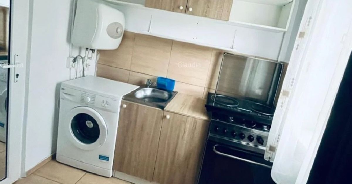 aspect din bucataria improvizata a unei garsoniere. in imagine se vad mai multe dulapuri si etajere alb si maro deschis, aragaz, chiuveta și o masina de spalat