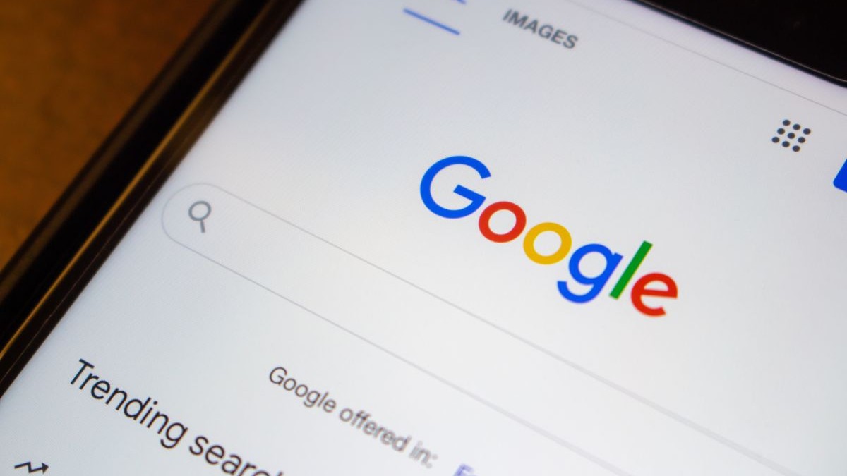 Logo-ul site-ului Google.com în prim-plan pe un iPhone așezat pe o masă de lemn.