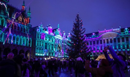 Vizitatorii, unii purtând măști de protecție, stau în fața bradului iluminat de la Winter Wonders, Bruxelles | Foto: Profimedia