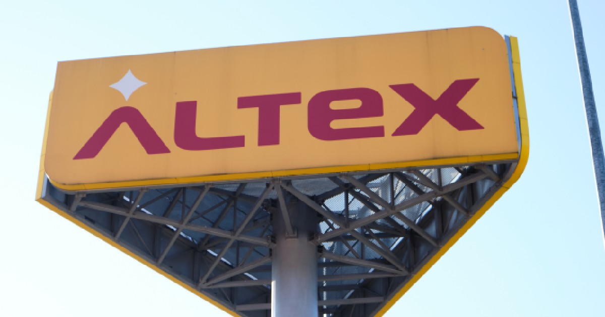 Imaginea prezintă o reclamă stradală de mari dimensiuni a retailerului român Altex, constând într-un panou galben cu logoul roșu al companiei, susținut de o structură metalică solidă pe un stâlp.