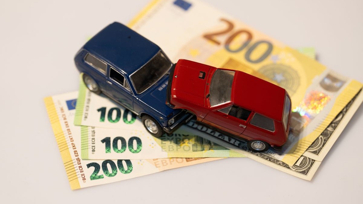 Imagine creativă cu două mașini de jucărie, una albastră și alta roșie, una peste alta, și împreună peste mai multe bancnote de 100 și 200 de euro