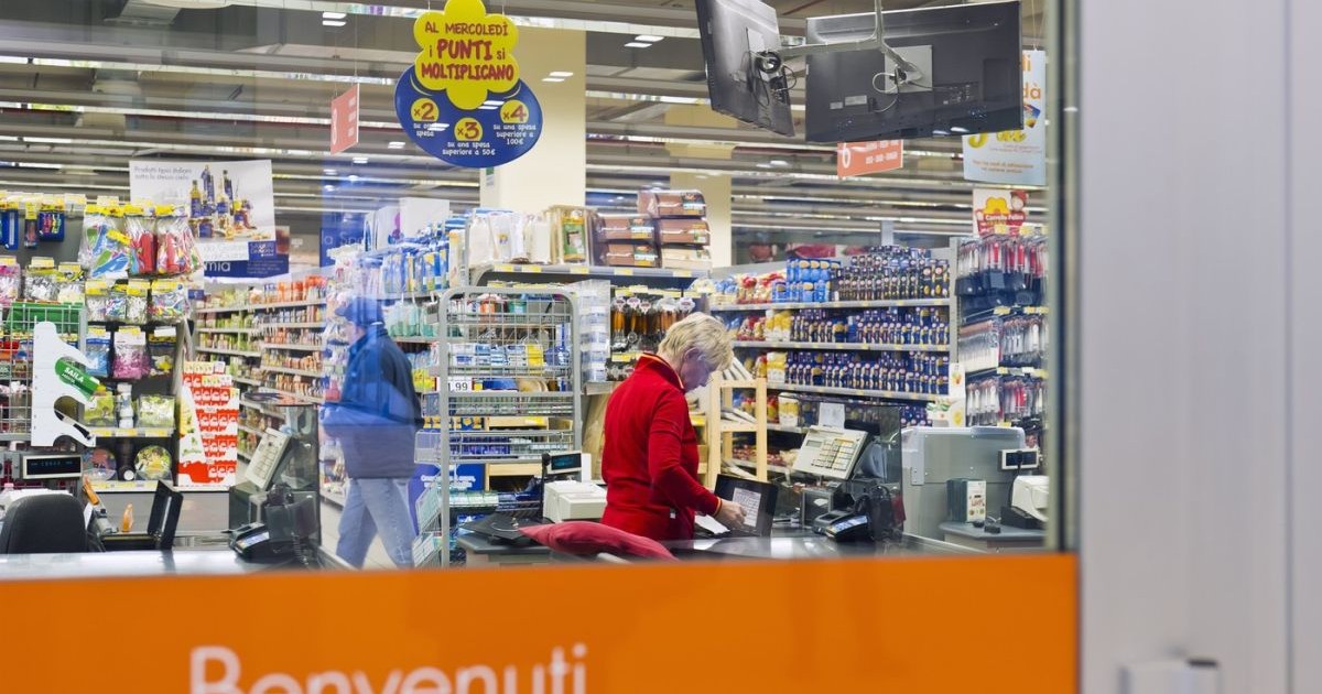 IUn bărbat se plimbă printre rafturi, în timp ce o angajată stă la casă și așteaptă clienții într-un supermarket din Italia, 8 mai 2022
