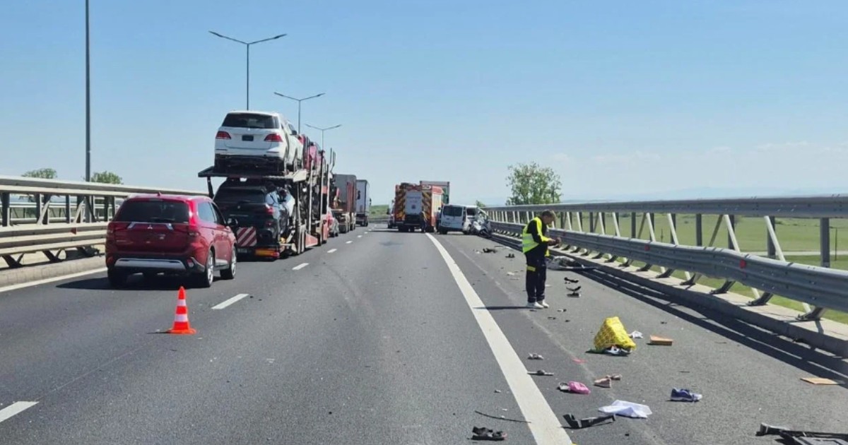 Locul unui accident rutier pe o autostradă, unde resturi de vehicule și obiecte personale sunt împrăștiate pe carosabil lângă un parapet metalic. În plan îndepărtat, o autospecială de pompieri și un vehicul avariat blochează drumul.