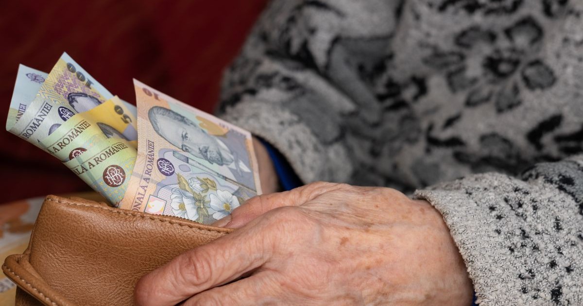 O bătrână cu pulover pe ea scoate dintr-un portofel maro, pe care îl ține cu o mână, câteva bancnote românești
