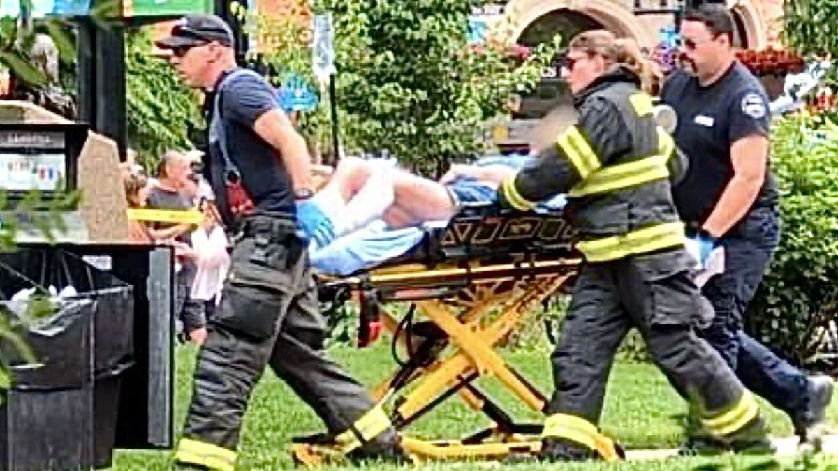 Doi oameni de la ambulanță și încă un bărbat cară pe targă un rănit, pe jos este iarbă și o zonă verde, Colorado, SUA, 2 iunie 2025