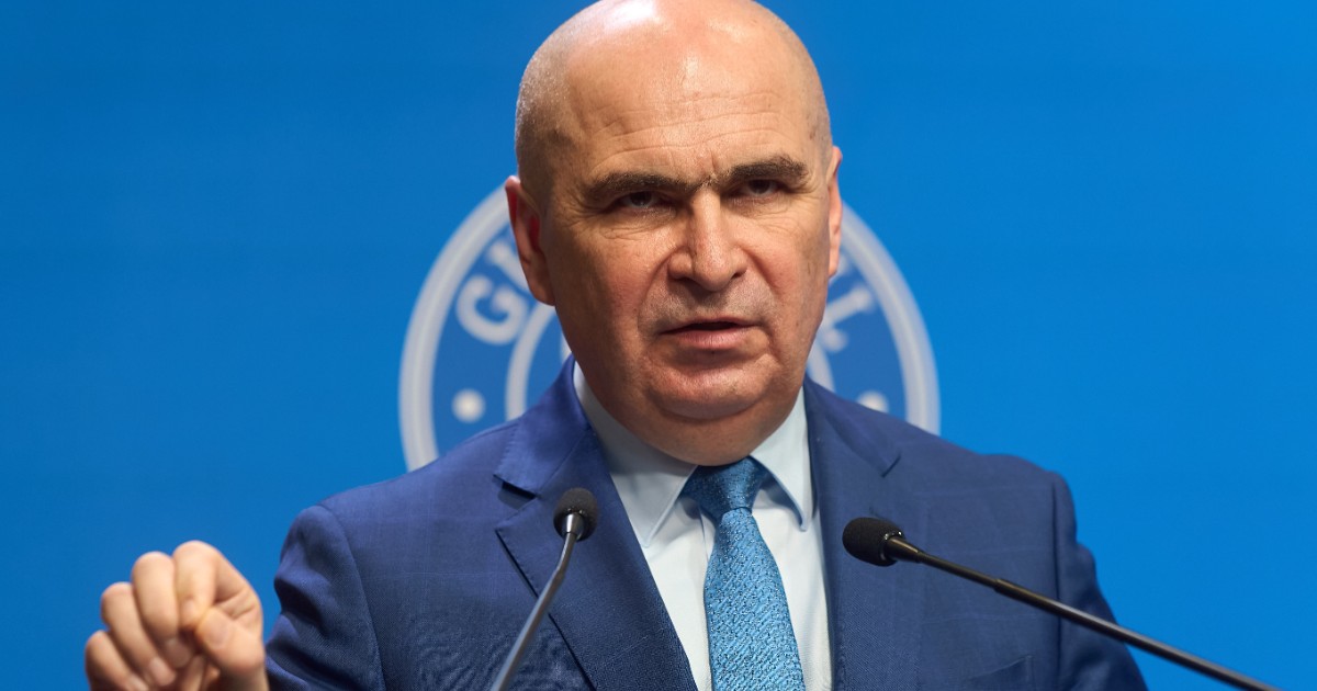 Ilie Boloajn îmbrăcat în costum albastru, gesticulând în fața unui microfon