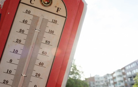 Un termometru de exterior în stil vintage, cu margine roșie, indicând o temperatură  de aproape 35°C în lumina soarelui.