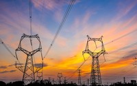 O rețea de energie cu stâlpi de curent de înaltă tensiune și cabluri interconectate, fotografiată într-o zonă de câmpie din România, la apus. Foto: Shutterstock