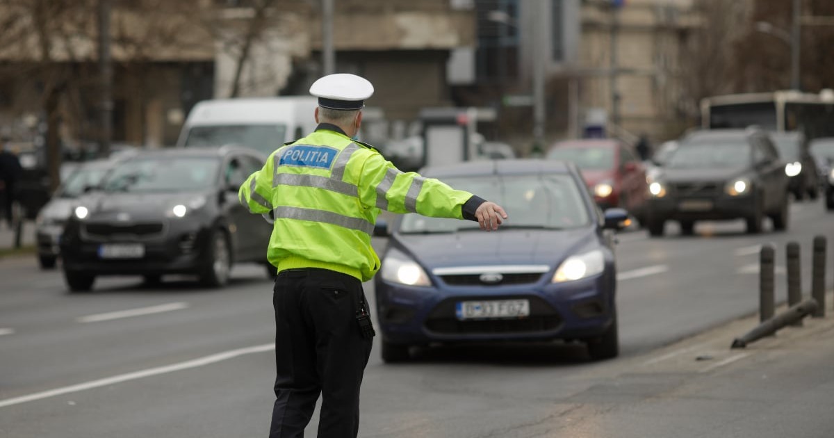 Un polițist rutier oprește traficul pe o stradă aglomerată, semnalizând unui șofer să tragă pe dreapta. În jur, mașinile circulă intens, sugerând o intervenție de rutină într-un oraș activ.