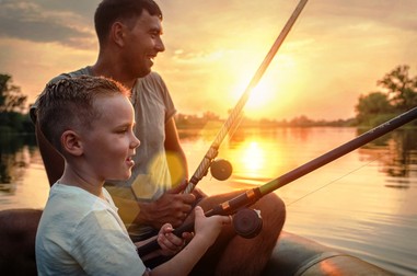 Happy Father and Son together fishing from a boat at sunset time in summer day under beautiful sky on the lake.
