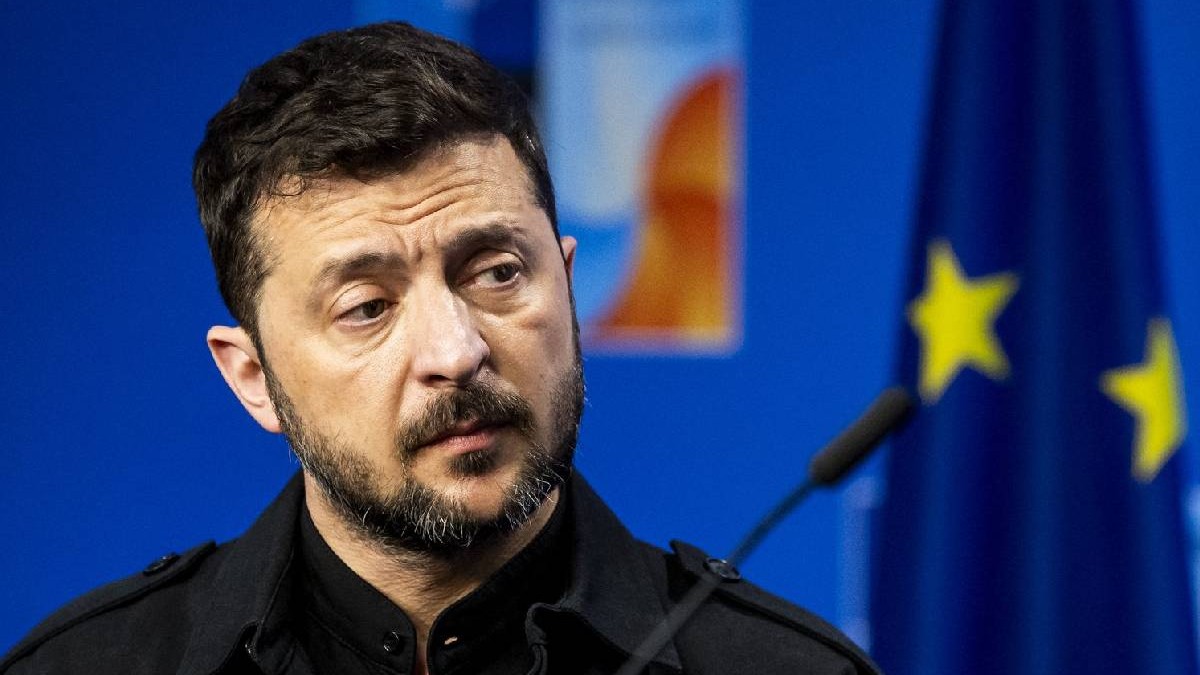 Președintele Volodimir Zelenski, îmbrăcat în negru, în timpul unei conferințe de presă, pe fundal se văd câteva stele de pe drapelul UE