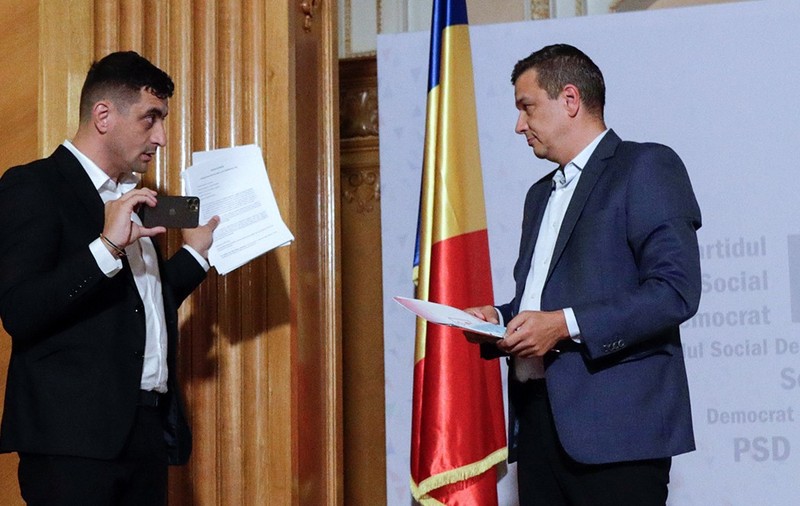 George Simion față în față cu Sorin Grindeanu, ambii cu documente în mână și îmbrăcați la costume de culoare închisă.