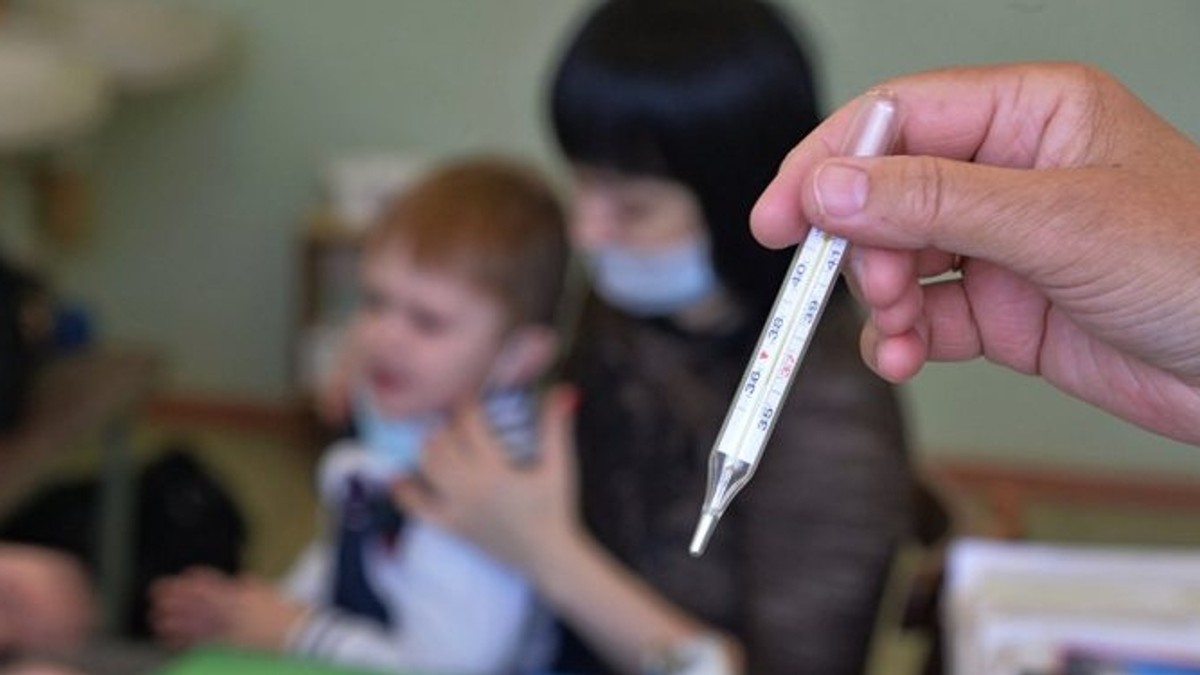 Ar putea să fie declarată epidemie de gripă în România. O mamă își ție copilul bolnav în brațe, în timp ce o asistentă medicală ține un termometru în mână