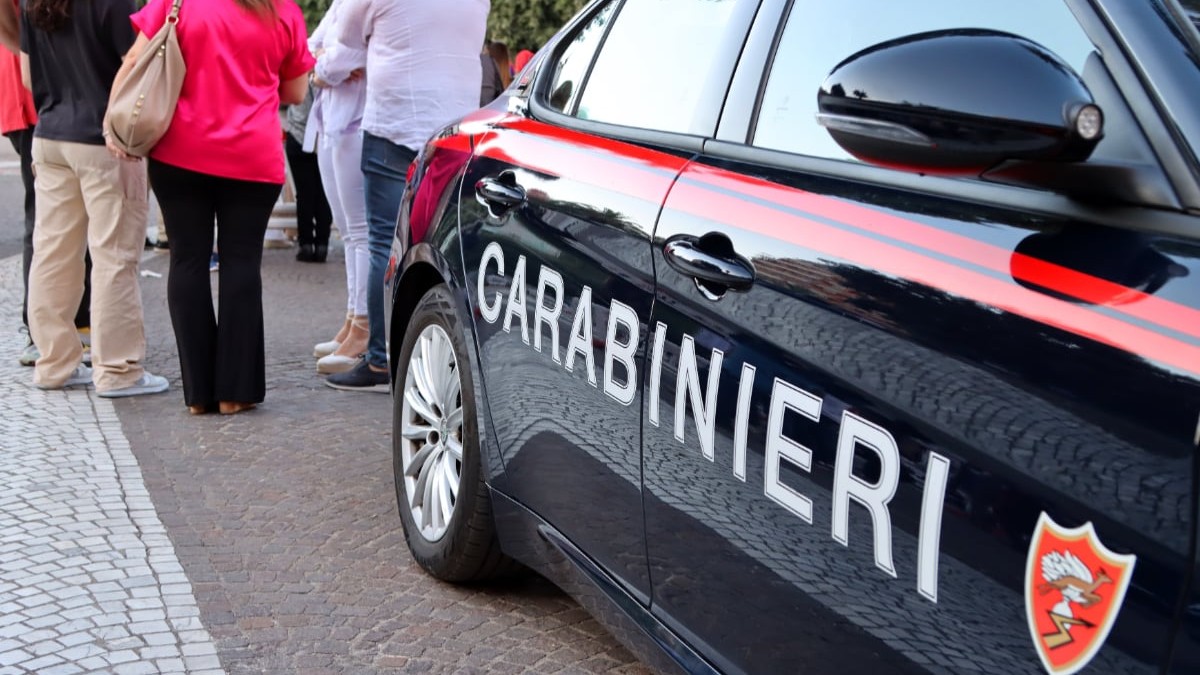 O mașină de carabinieri lângă care se află mai mulți oameni.