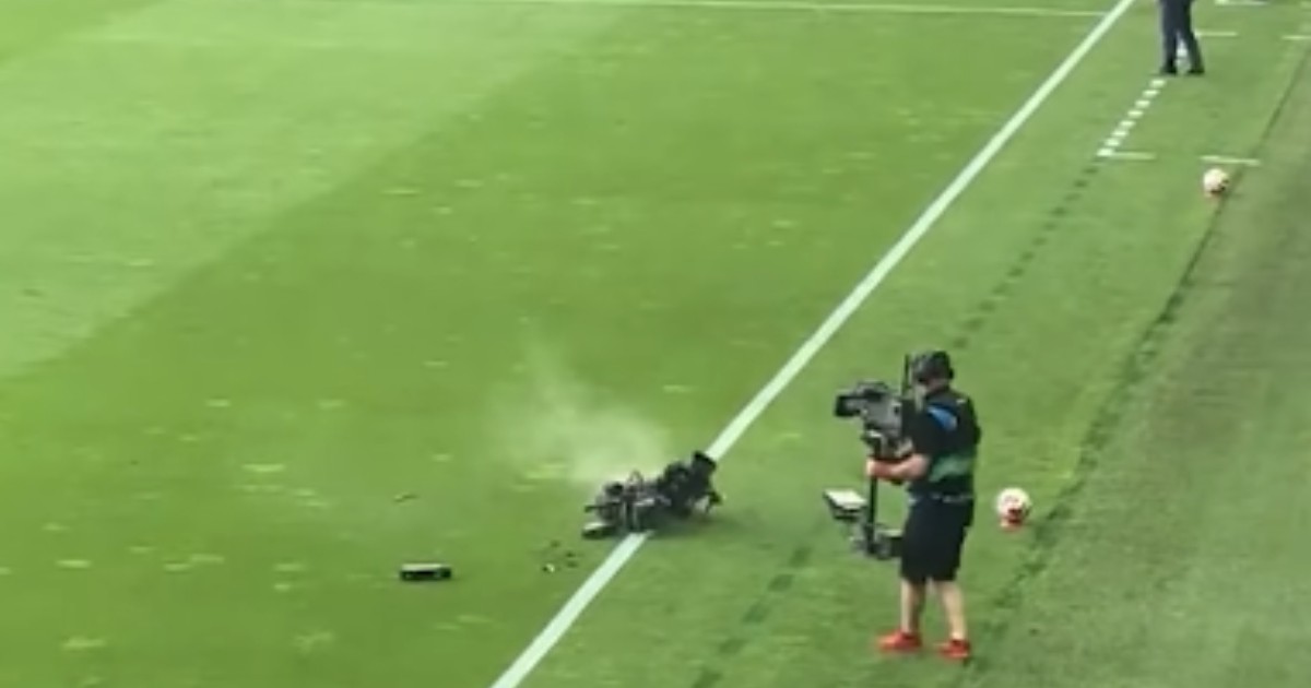 Un cameraman pe terenul de fotbal, aflat lângă o cameră care a luat foc