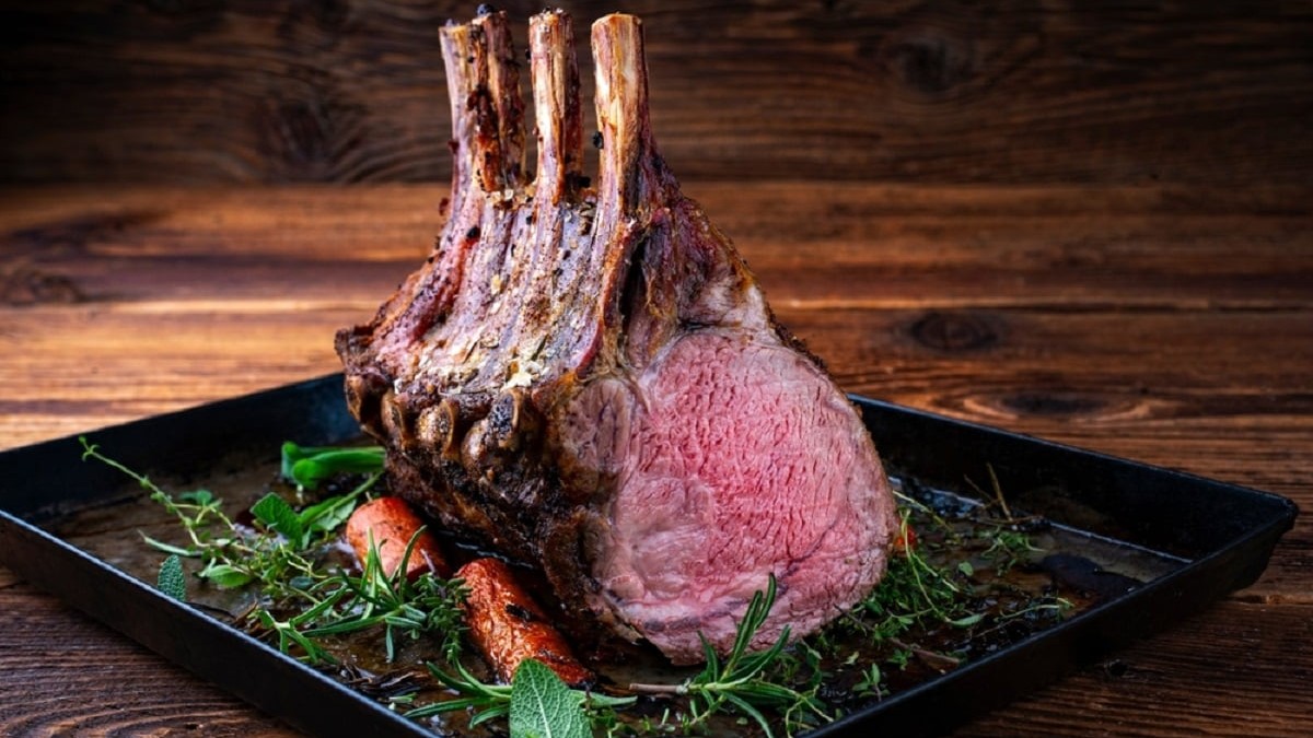 Cum să alegi cea mai bună carne pentru friptura de duminică - Imagine cu coaste de vițel cu os, maturate la uscat, coapte cu ierburi și condimente, servite pe o tavă neagră