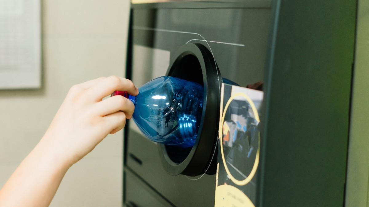 O mână care introduce o sticlă din plastic într-un aparat automat pentru colectarea și reciclarea ambalajelor.