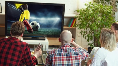 Friends, men and women gathering at home to watching online football match translation. Eating snacks, drinking beer