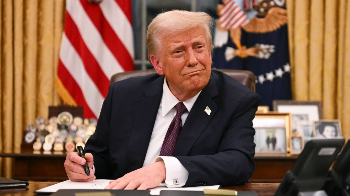Donald Trump, îmbrăcat în costum, în timp ce stă la Biroul Oval, la Casa Albă, și semnează un document, în ianuarie 2025