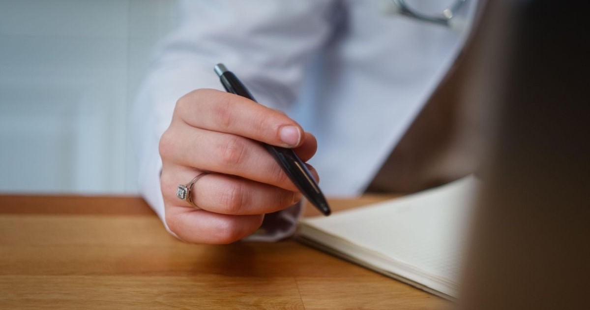 O doctoriță ține un pix în mâna dreaptă, în timp ce consultă o agendă