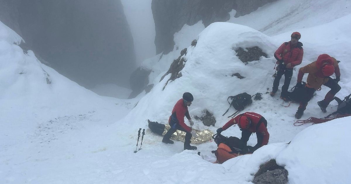 Imaginea arată o intervenție de salvare montană într-o zonă abruptă, acoperită de zăpadă și ceață densă montană abruptă