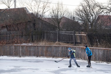 Doi copii joacă hockey pe un patinoar artificial în spatele căminului cultural din Ditrău.