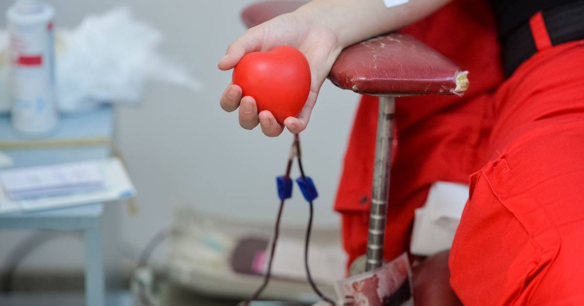 persoana care doneaza sange. Mâna este sprijinită pe manerul scaunului, tinand strans o perna in forma de inima