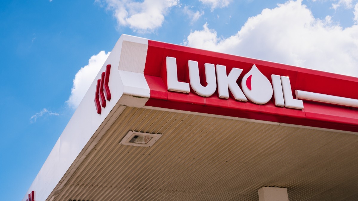 Logo-ul Lukoil cu alb, pe o suprafață roșie. În fundal, cerul este senin.