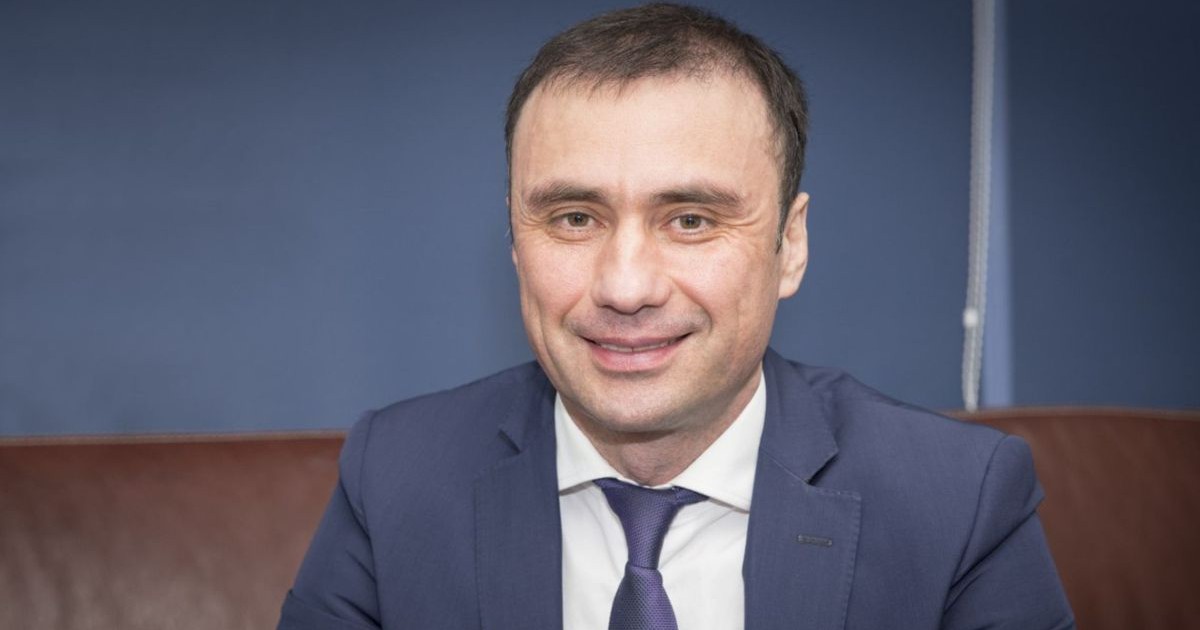 Vitalie Pirlog, directorul Serviciului de Informații și Securitate al Republicii Moldova, fost ministru al justiției în guvernul Partidului Comunist, stă pe o canapea îmbrăcat în costum gri și cămașă albă, zâmbește în fața camerei de filmat