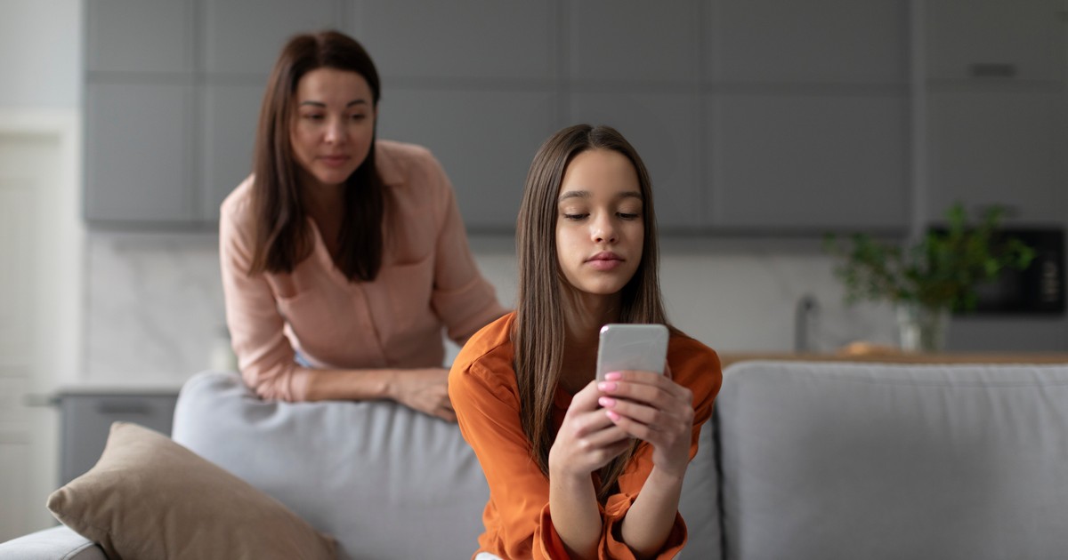 O mama incearca sa se uite la ce scrie fiica sa pe telefon, din spatele ei.