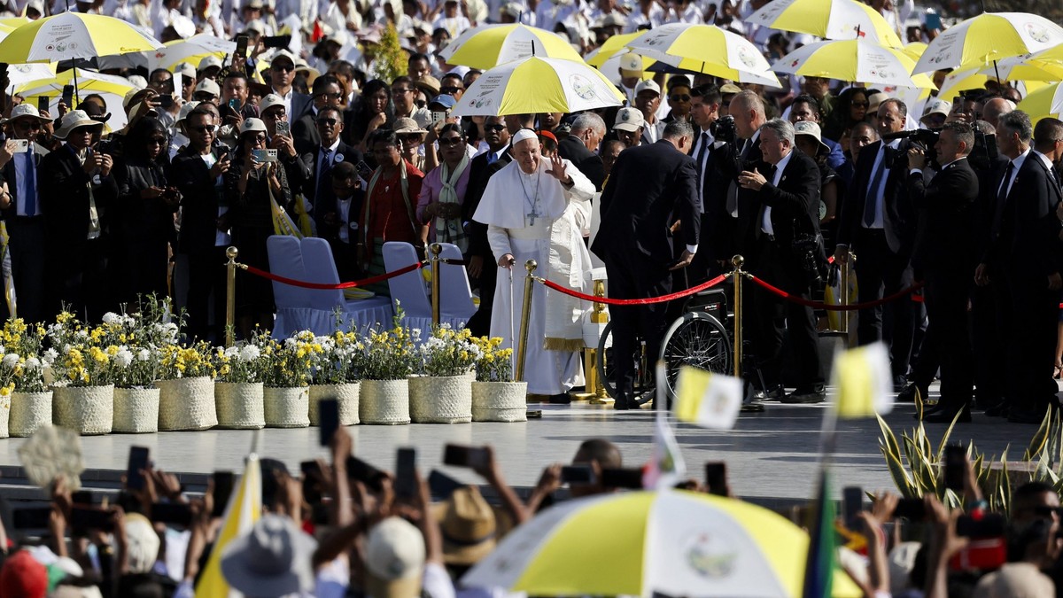 Papa Francisc în mijlocul imaginii, în timpul vizitei sale în Timorul de Est, ținând o umbrelă în culorile naționale ale statului asiatic.