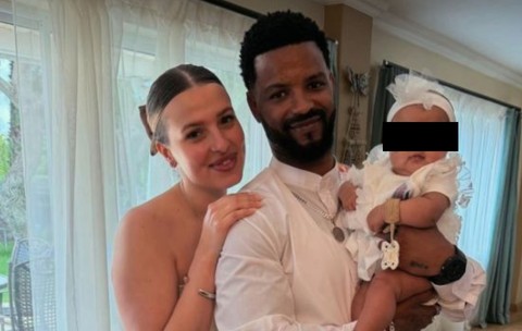 O familie formată din soț și soție, mândoi îmbrăcați în alb, în timp ce țin un bebeluș în brațe