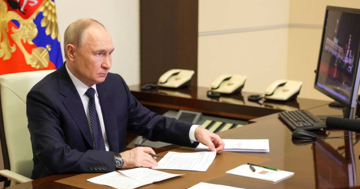 Vladimir Putin în biroul său, stând în fața unui monitor și notând ceva pe o hârtie.