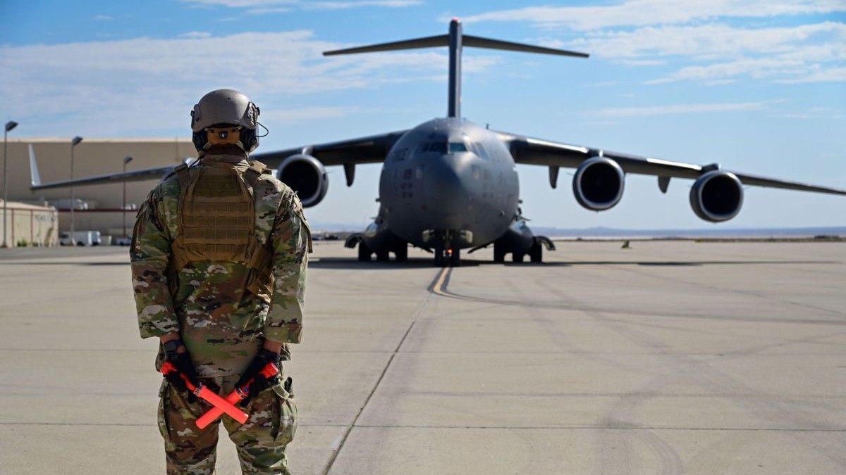 avion militar C-17 al SUA, folosit pentru deportări, în spate, cu un militar american în față.