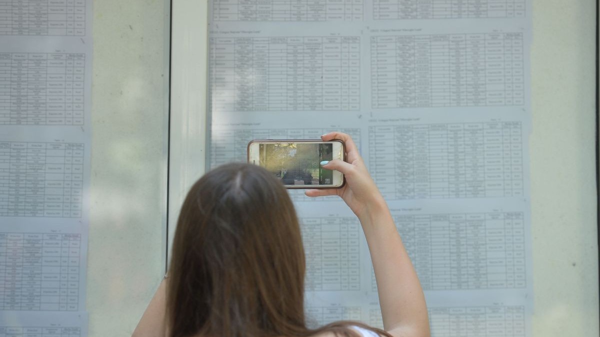 O fată fotografiază panoul după afișarea rezultalelor la examen