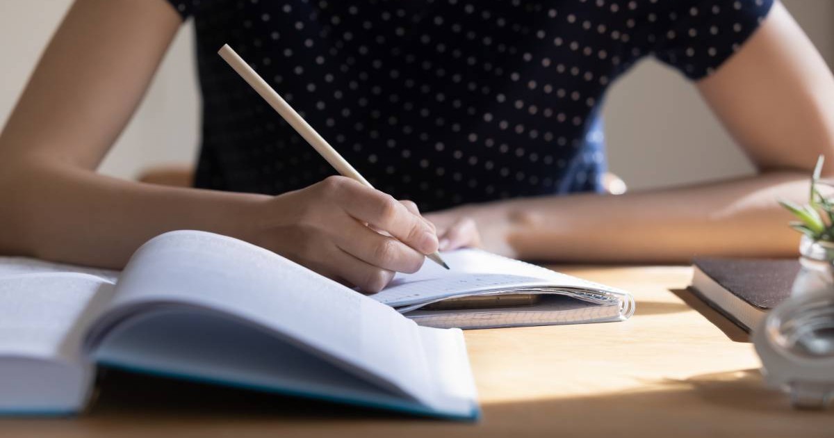 studentă care se pregătește pentru testul de facultate, examen, își ia notițe, face schițe, rezumatul manualului, studiază, citește o carte pentru raportul de curs. Prim-planul mesei de lucru pentru învățare